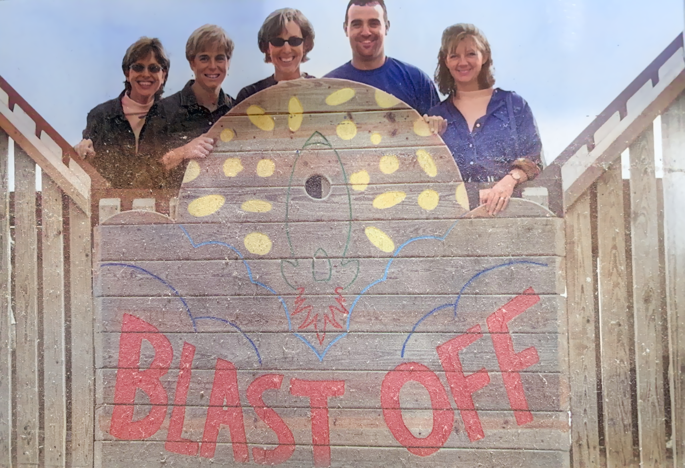 Volunteers pose in front of the newly built Blast Off Playground sign